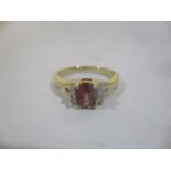 A gold coloured ring set with an oval cut red sapphire approximately 0.8ct flanked by six