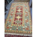 A Turkish hand woven red and beige ground rug having geometric designs and tasselled ends 218cm x