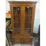 A reproduction oak glazed two door display cabinet with two drawers below and on bracket shaped feet