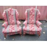A pair of early 20th century wing back upholstered armchairs, upholstered in a floral red fabric