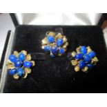 A gold coloured ring fashioned as a flower with textured leaves set with blue cabochons, together