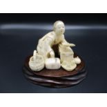 A Japanese Meiji period ivory okimono, modelled as a scholar reading a book, on a carved wooden