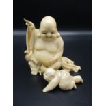 A Japanese Meiji period ivory okimono, modelled as Hotei the laughing Buddha, playing with an