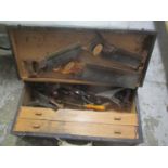 A vintage toolbox containing woodworking planes, saws, drill pieces and other items