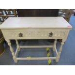 A distressed cream painted side table with twin drawers, on turned block legs