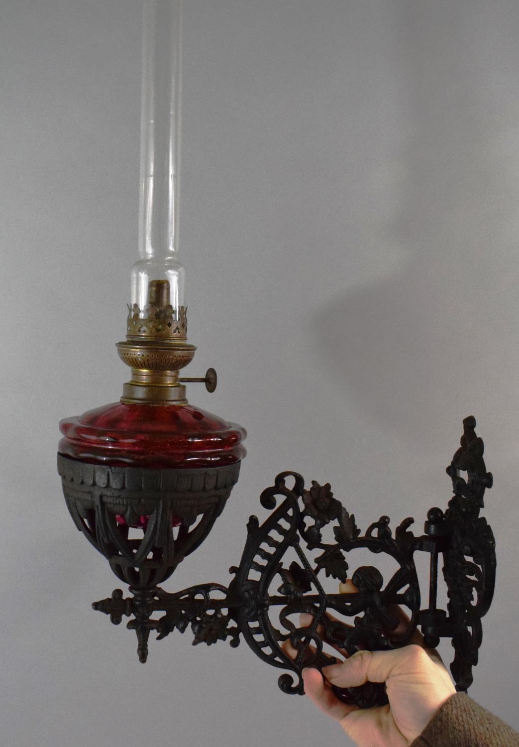 A Victorian Pierced Metal Wall Mounting Oil Lamp Holder Complete with Lamp Having Cranberry Glass