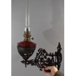 A Victorian Pierced Metal Wall Mounting Oil Lamp Holder Complete with Lamp Having Cranberry Glass