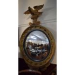 A Regency Style Gilt Convex Wall Mirror with a Spread Eagle Supported on a Scrolled Plinth and