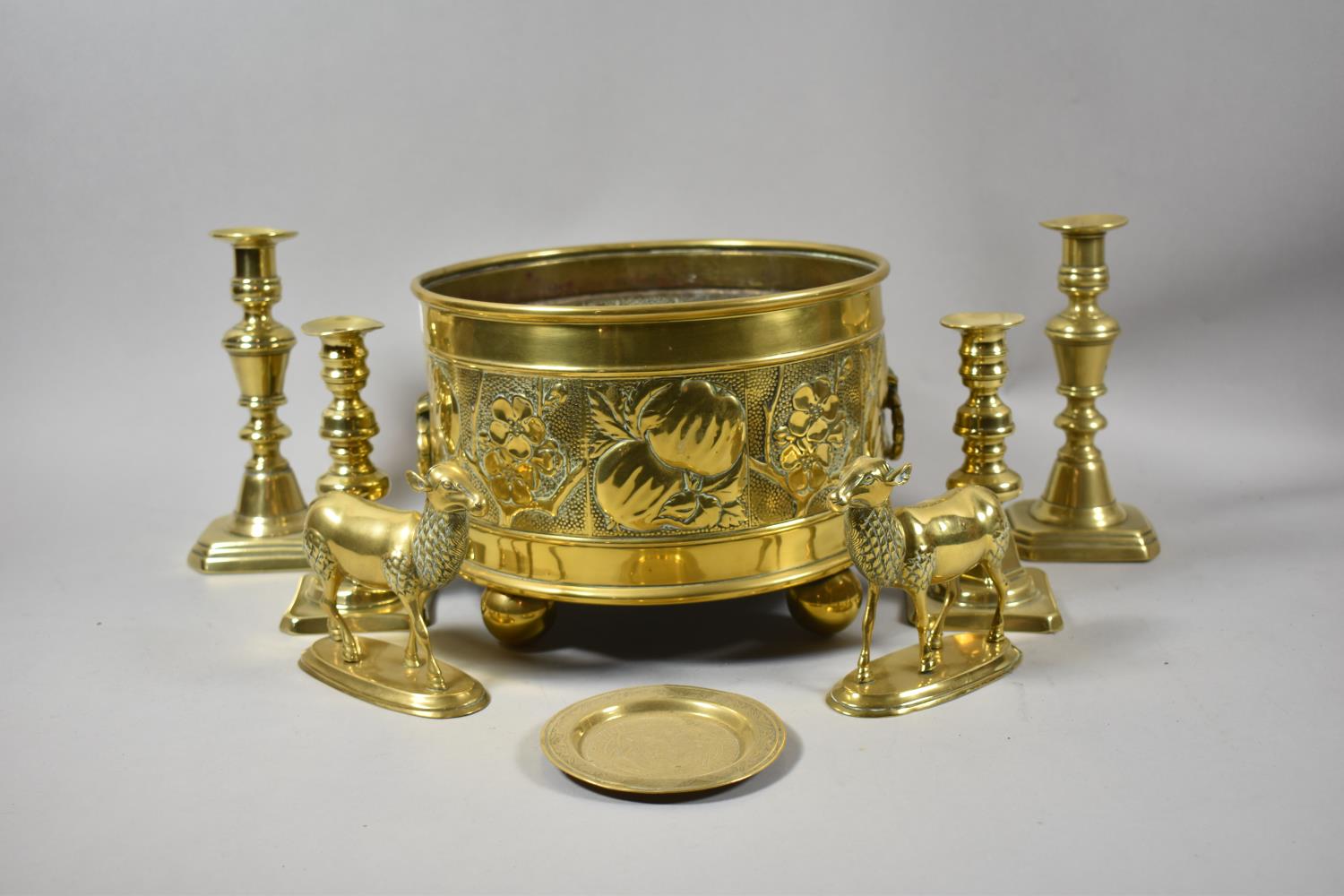 A Circular Brass Bowl with Repousse Fruit Decoration and Oval Ring Carrying Handles on Four Ball