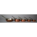 A Graduated Set of Four Copper Miniature Saucepans and a Larger Frying Pan