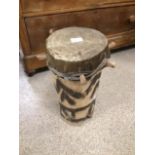 A VINTAGE AFRICAN TRIBAL WOODEN DRUM WITH DETAILING ON THE SIDE, A HIDE TOP, AND DECORATIVE WOODEN