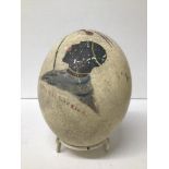 AN UNUSUAL EARLY 20TH CENTURY PAINTED OSTRICH EGG DEPICTING A MATABELLE WARRIOR, SIGNED AND DATED MW