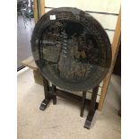 A TILT TOP ROUND TABLE WITH A CARVED ORIENTAL SCENE TO THE TOP IN A GLASS SURROUND