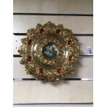 AN ORNATE GILDED BRASS WALL PLAQUE FROM ITALY (REGISTRATION) WITH A PICTURE TO THE MIDDLE 27CM