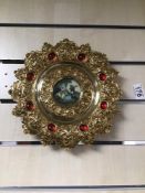 AN ORNATE GILDED BRASS WALL PLAQUE FROM ITALY (REGISTRATION) WITH A PICTURE TO THE MIDDLE 27CM