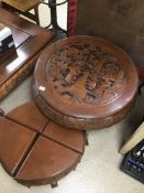 A HARD WOOD ORIENTAL CARVED SCENES ROUND TABLE WITH A NEST OF FOUR UNDER SIDE TABLES