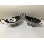 A PAIR OF EDWARDIAN HALLMARKED SILVER OVAL & TWIN HANDLED PEDESTAL SALTS WITH BLUE GLASS LINERS BY