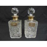 A pair of cut glass silver mounted decanters with silver wine labels and faceted drop stoppers