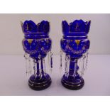 A pair of blue glass lustres decorated with flowers, leaves and gilded borders on raised circular