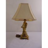 A gilded metal table lamp in the form of a putti on raised circular base with silk shade