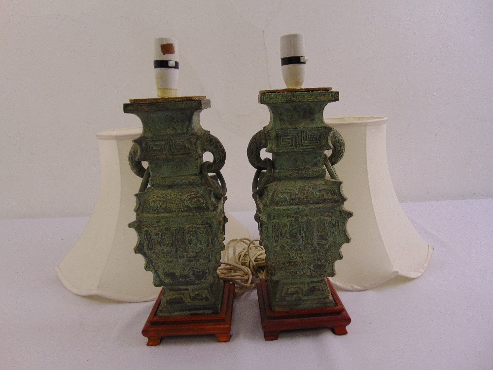 A pair of Chinese style bronze table lamps on raised wooden plinths with silk shades
