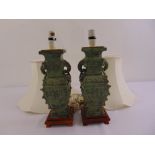 A pair of Chinese style bronze table lamps on raised wooden plinths with silk shades