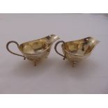 A pair of silver sauce boats with reed and tie borders, scroll handle and panelled sides on three