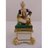 An early 19th century Royal Crown Derby figurine of an Arabian gentleman seated on a pillow