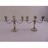 A pair of three branch silver squat candelabra, tapering cylindrical stems supporting scrolling arms