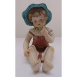 A bisque porcelain figurine of a seated child wearing a sun hat, 30cm (h)