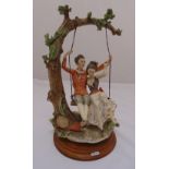 A Capodimonte figural group of lovers on a swing, on raised circular wooden plinth, 43cm (h)