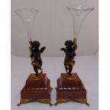 A pair of cast bronze putti supporting glass vases on raised square marble bases with gilt metal