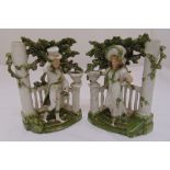 A pair of Staffordshire ceramic figurines of a lady and gentleman in formal attire in a leafy bower,