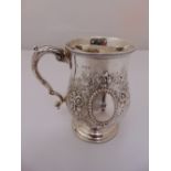 A Victorian silver mug with floral and foliate raised body, scroll handle and pedestal base,