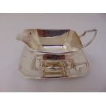 Silver sauce boat, rounded rectangular on hoof feet and scroll handle on shaped rectangular base