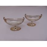 A pair of oval silver pierced bonbon dishes with leaf scroll side handles on raised oval bases,