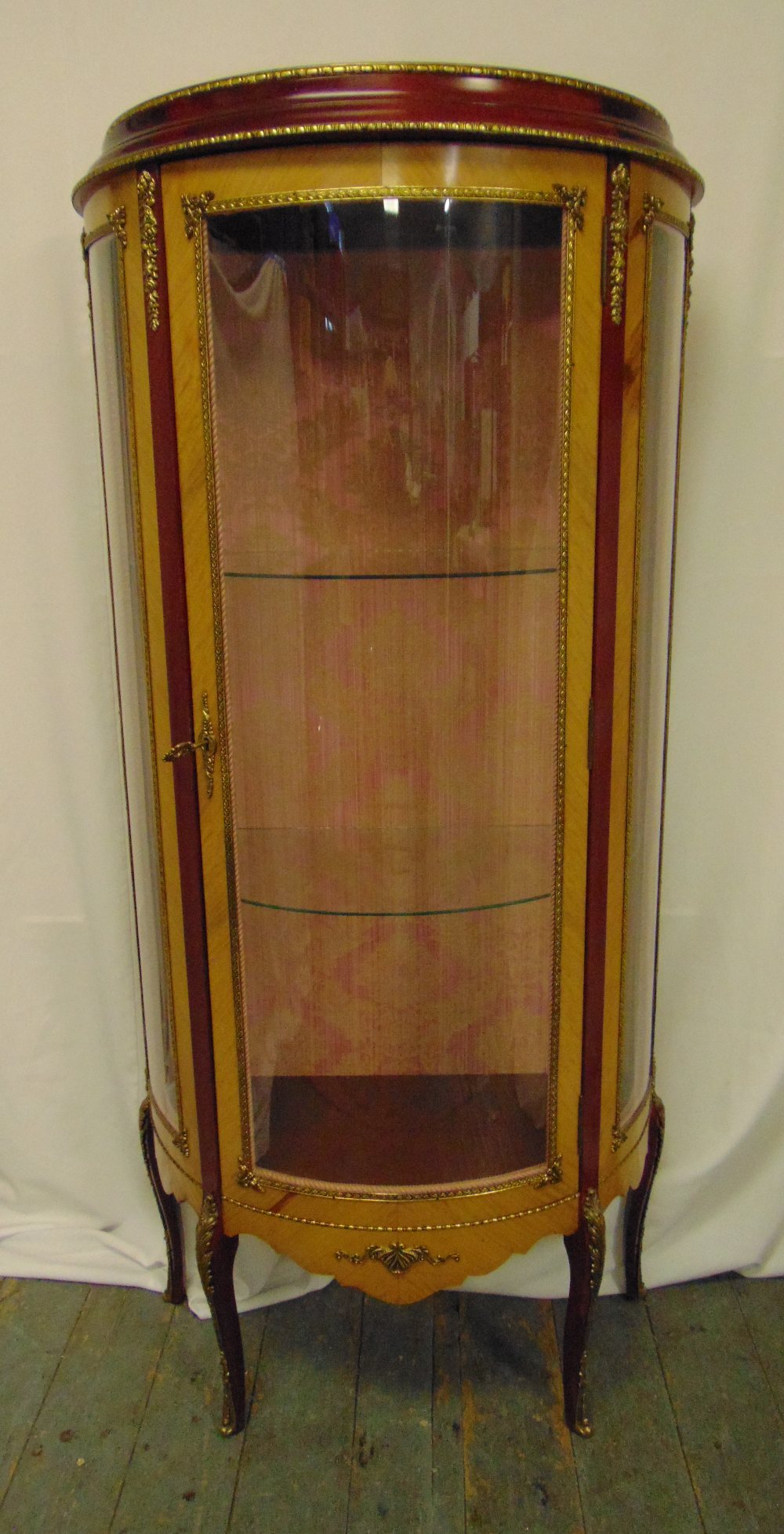 A continental glazed display cabinet of cylindrical form with gilt metal mounts, hinged door on four