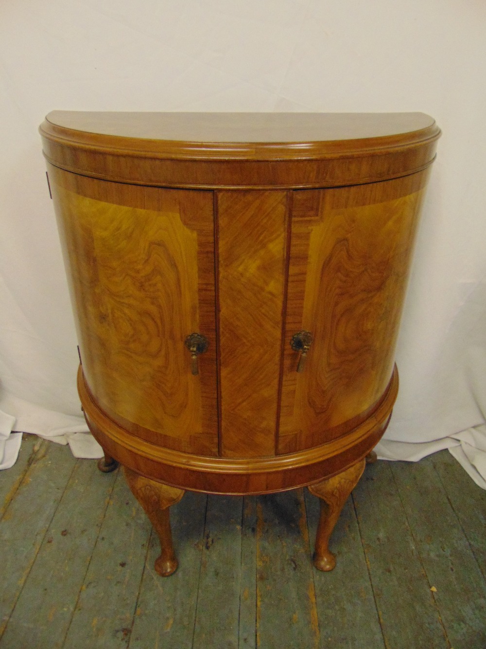 A mahogany and satinwood demi-lune cabinet with hinged doors on four scroll legs, 99 x 78 x 38.5cm