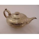 A George IV silver teapot of compressed circular form engraved with leaves scrolls and flowers,