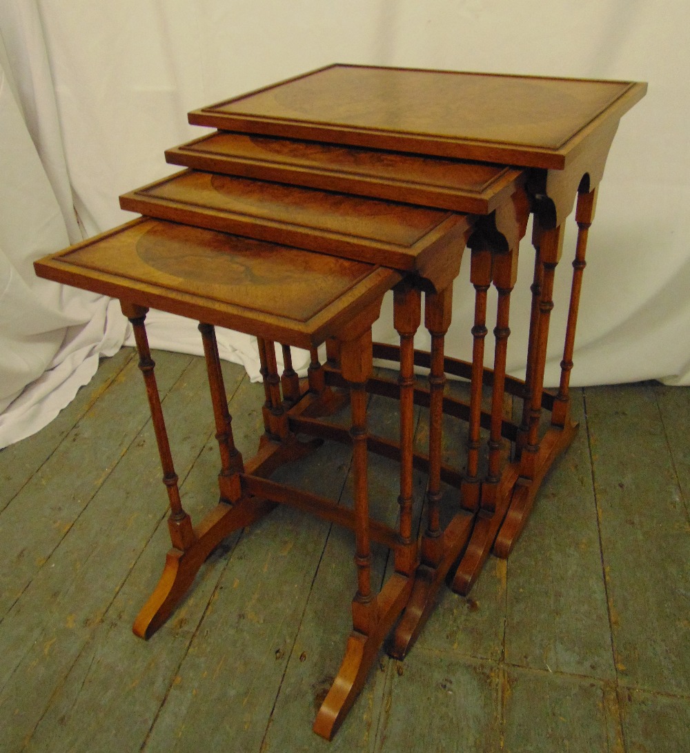 A nest of four rectangular burr walnut side tables on turned tubular supports and outswept bracket