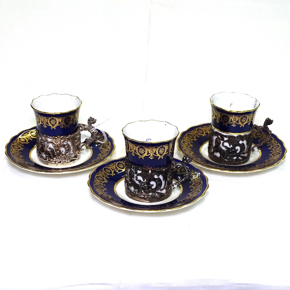 A set of 3 Edwardian Coalport porcelain cups and saucers, in pierced hallmarked silver holders