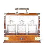 A Victorian oak tantalus with electroplate mounts, containing 3 original square cut-glass decanters,