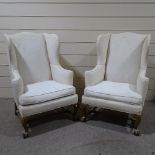 A pair of Queen Anne style upholstered wing armchairs, on carved walnut bases with ball and claw