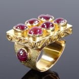 An Eastern unmarked gold cabochon ruby cluster panel ring, scrollwork border and ribbed cabochon