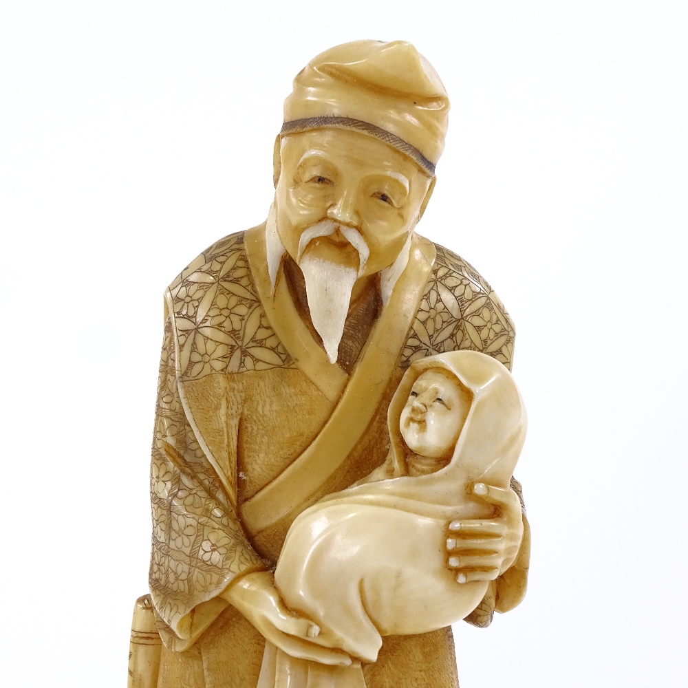 A Japanese 2-tone stained ivory okimono, man carrying an infant, Meiji period, signed under base,