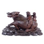 An Oriental hardwood figure of 2 boys riding a water buffalo, on fitted carved and pierced stand,