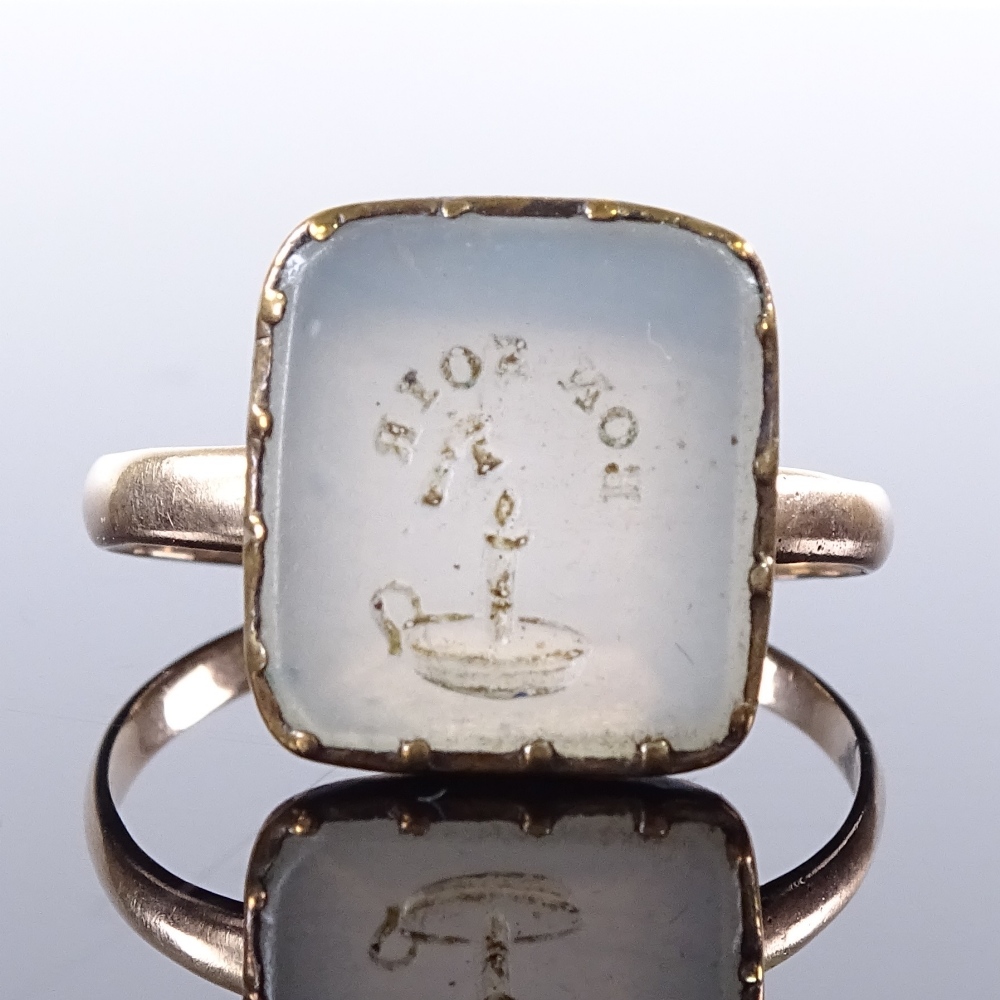 An unmarked yellow metal intaglio carved Bon Soir chalcedony panel seal ring, with chamber stick