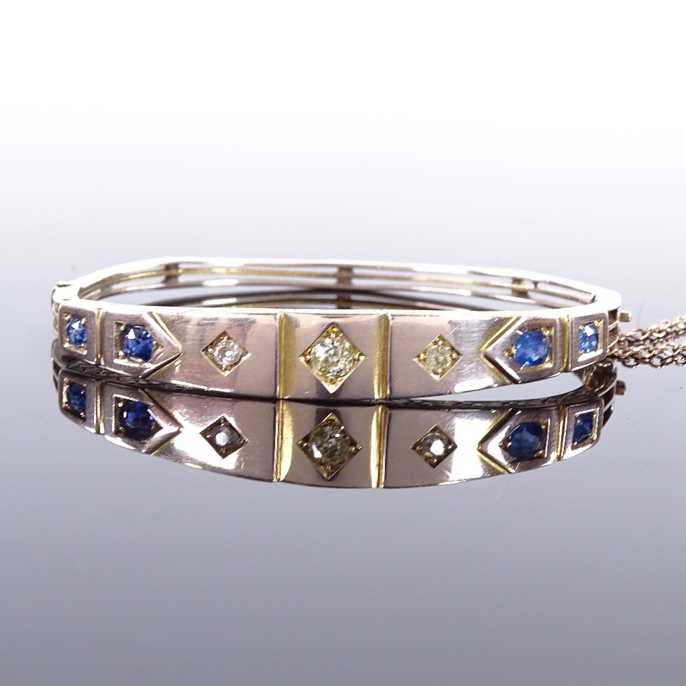 A Victorian unmarked gold sapphire and diamond hinged bangle, floral engraved bridge, total