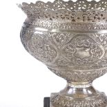 A large unmarked Indian silver fruit bowl on plinth, heavy relief embossed floral decoration with