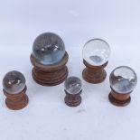 A graduated set of 5 clear glass crystal balls on wood stands, largest and smallest diameters 10cm